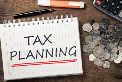 A notebook with "tax planning" written on it next to a pile of coins and a calculator.