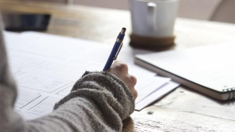 A woman sitting at a desk holding a pen and reviewing paperwork.