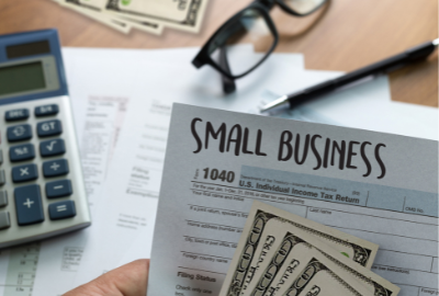 A hand holding a 1040 form and three $100 bills.