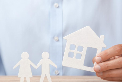 A hand holding a white silhouette of a house with a white male and female silhouette holding hands next to the home.