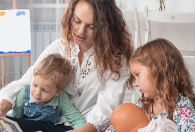 A Caucasian woman reading a book to a young boy and girl.