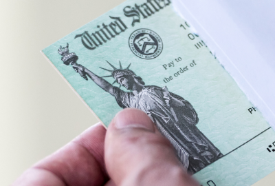 A hand pulling a US government check out of an envelope.
